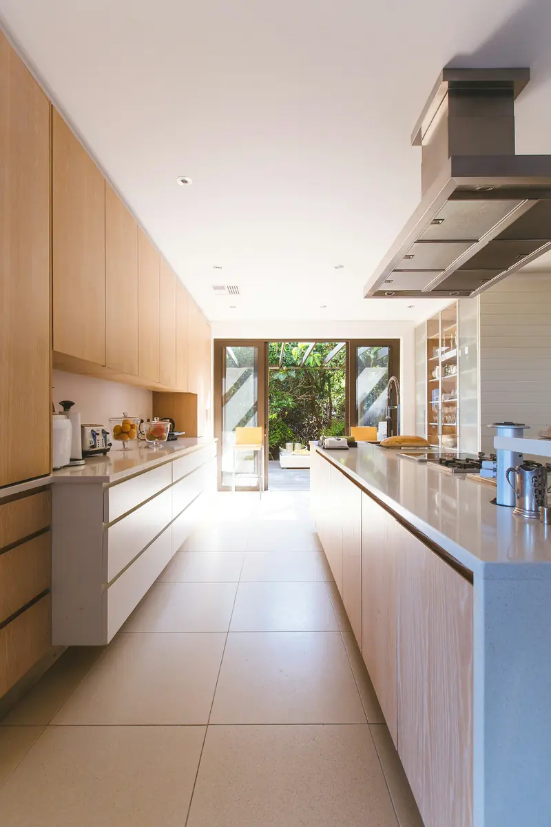 Cocina lineal en madera con encimera clara y salida al patio