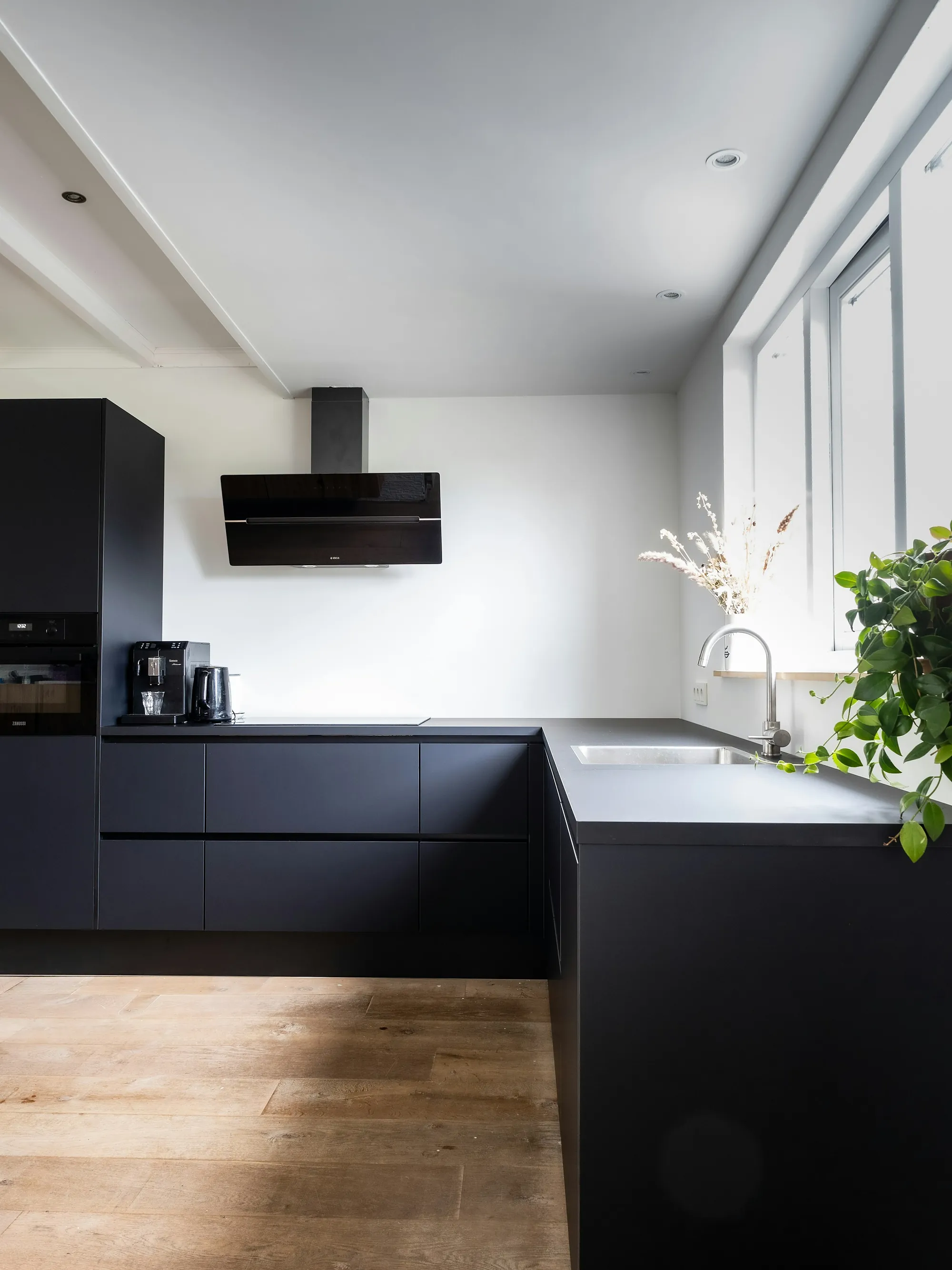 Cocina en negro mate con encimera blanca y suelo de madera